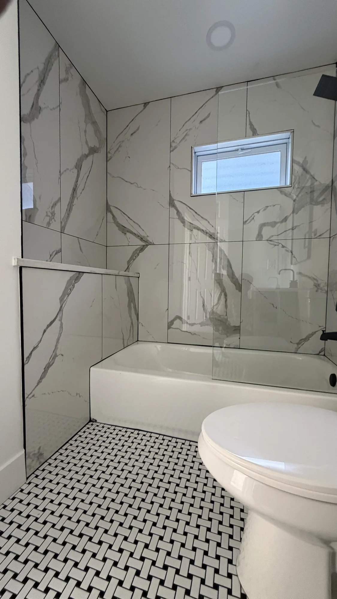 Bathtub with large-format marble-look tile and basketweave floor